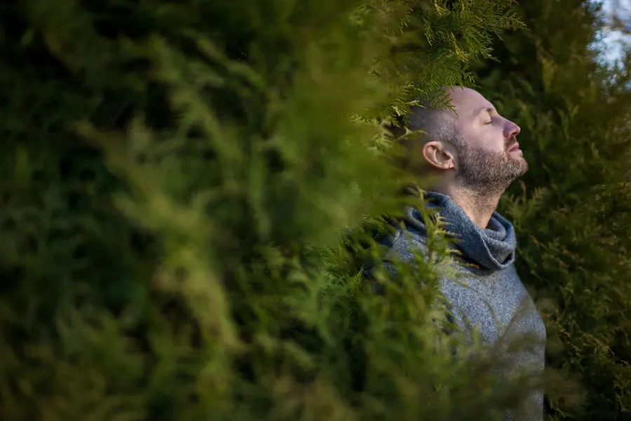 Man with eyes closed, present among greenery