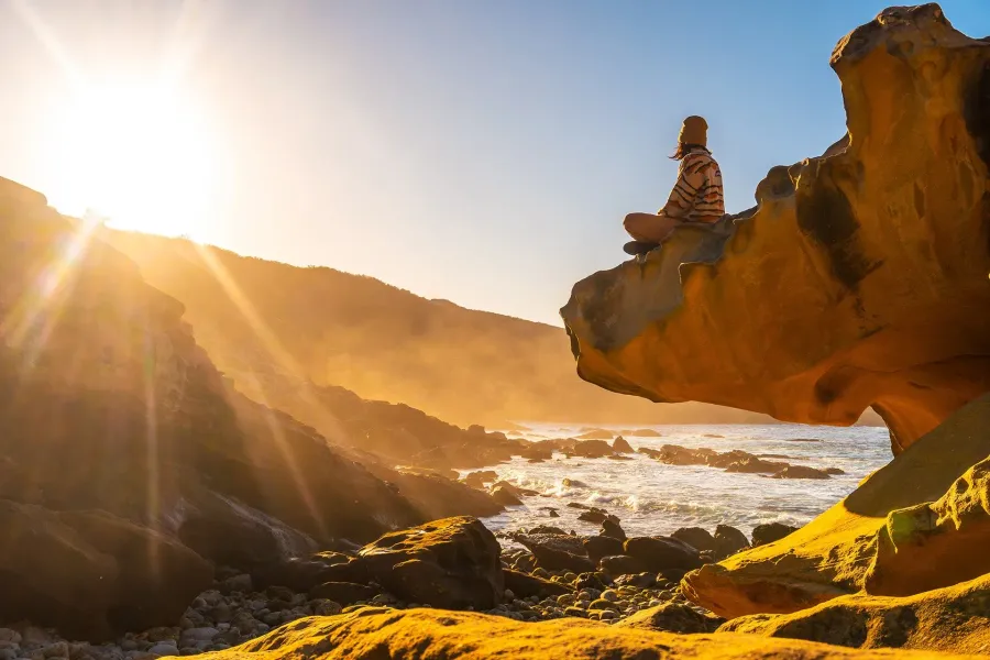 Person sitting on a rock overlooking the sea at sunset