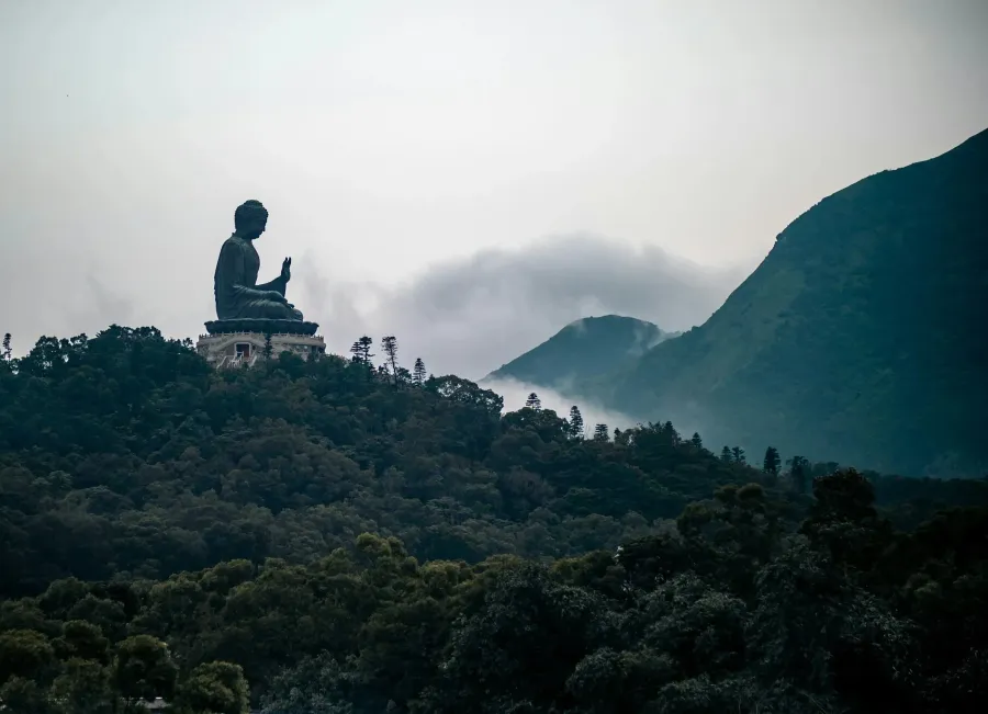 Large seated Buddha statue on a hilltop surrounded by mist and mountains