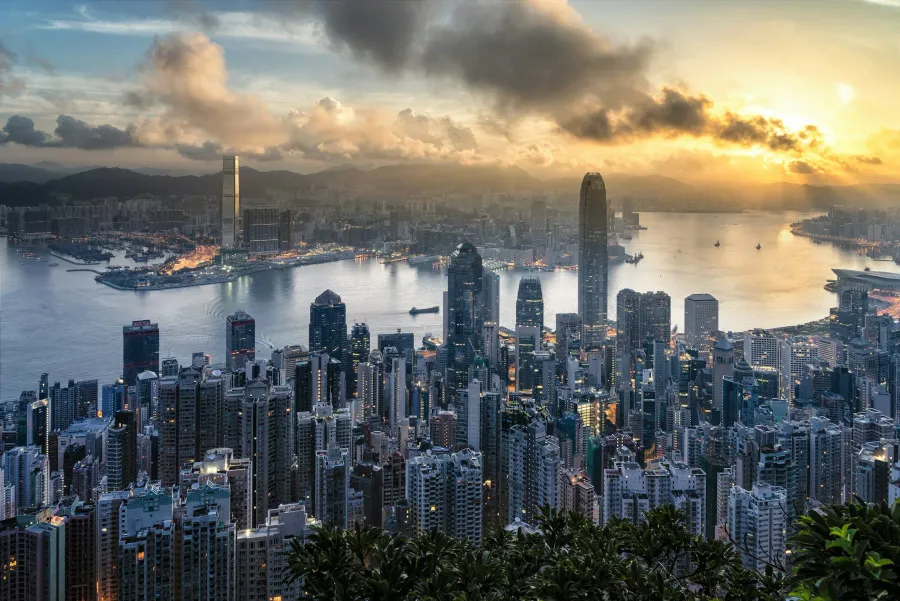 City skyline at sunset with tall skyscrapers, a river, and mountains